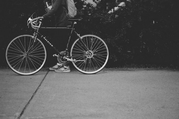grayscale photo of person holding a bicycle
