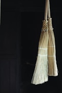 Traditional brooms with natural bristles standing against a rustic wall.