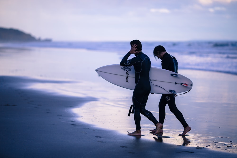 person walking on seashore holding surfboard