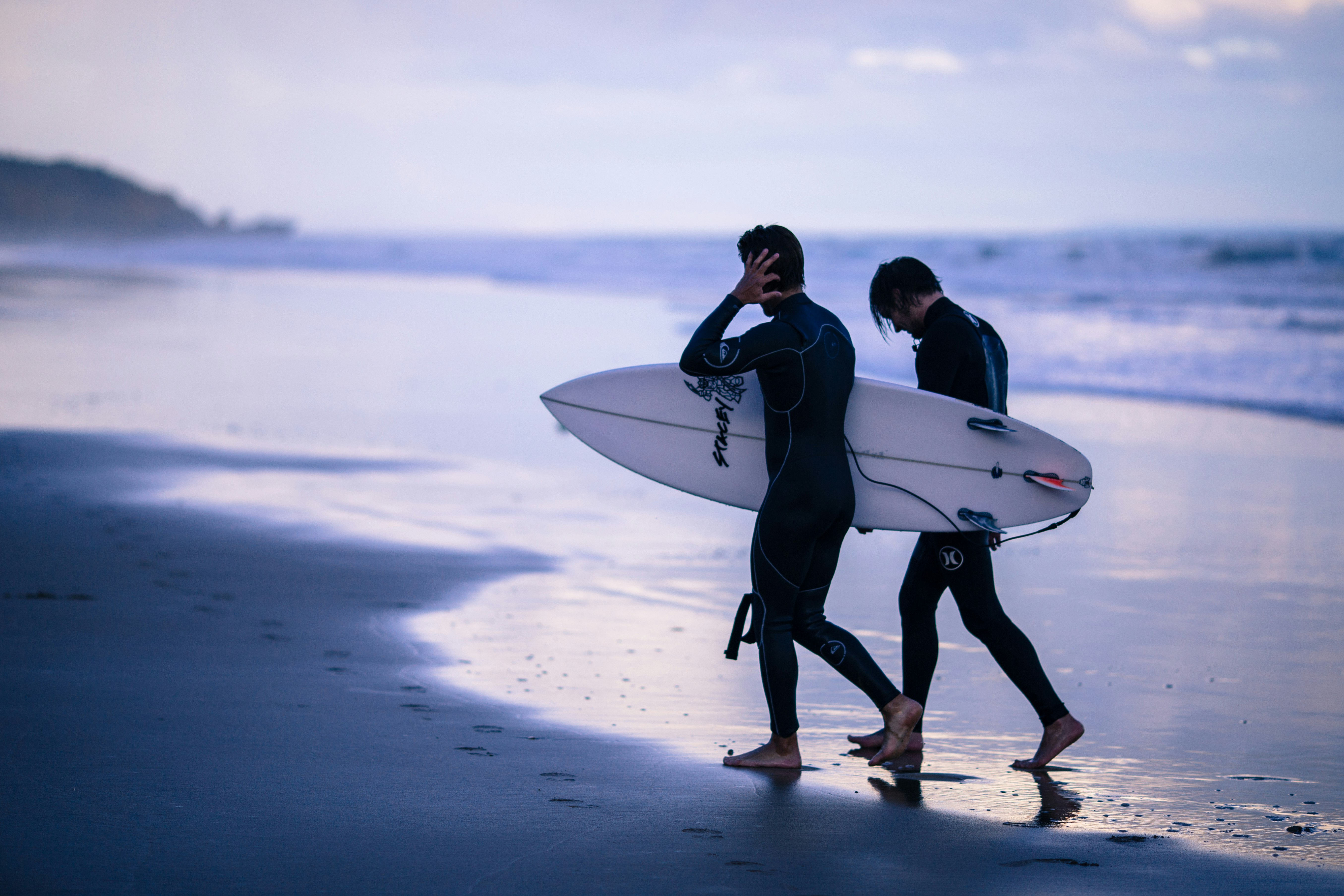 person walking on seashore holding surfboard