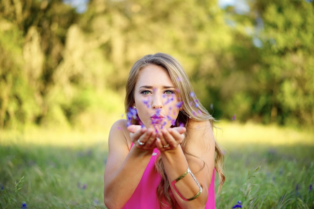 woman wearing pink sleeveless top blowing purple flowers