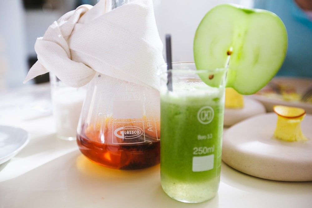 a green liquid in a glass next to an apple