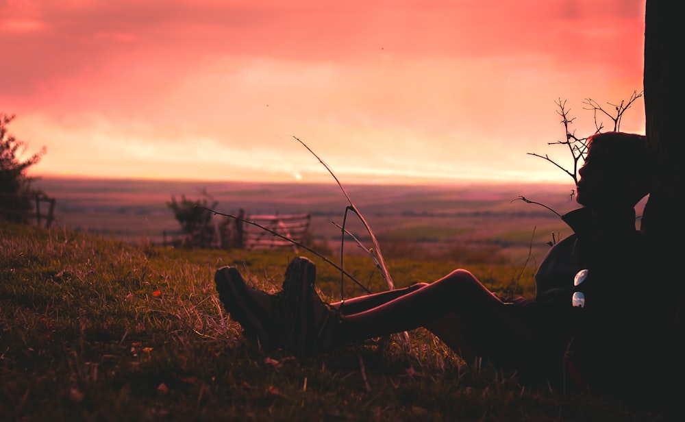 silhouette of person sitting on green grass during golden hour