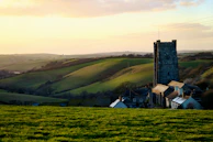 A peaceful countryside scene with rolling green hills and a charming stone cottage bathed in golden afternoon light.