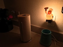 A dimly lit kitchen counter with a roll of paper towels, a blue appliance, and a plug-in night light featuring a chef figurine holding a pizza.