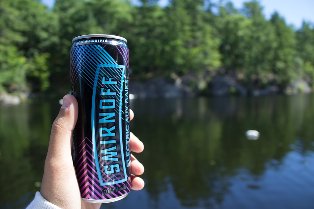 a person holding a can of water near a lake