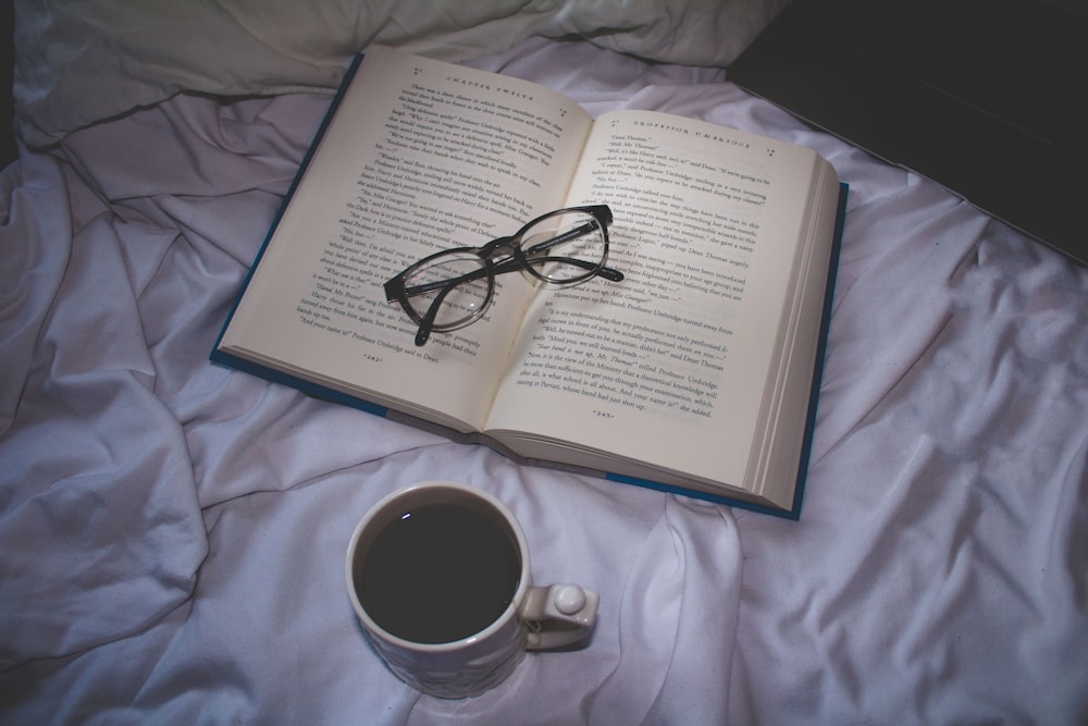 眼鏡をかけた開いた本の近くでコーヒーを飲む