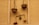 A rustic wall features traditional balance scales hanging vertically. The scales are made of rough, woven materials. One scale holds a variety of colorful fruits, while the other appears empty. The arrangement is simple, with a branch supporting a small plant and the balanced fruits.
