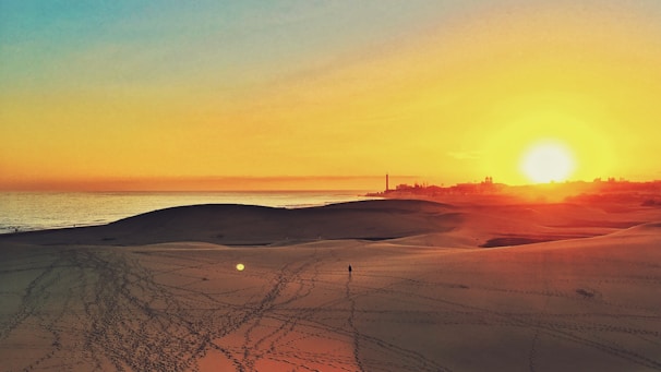 Sunset over the vast, golden dunes of the Sahara Desert with a lone traveler walking.