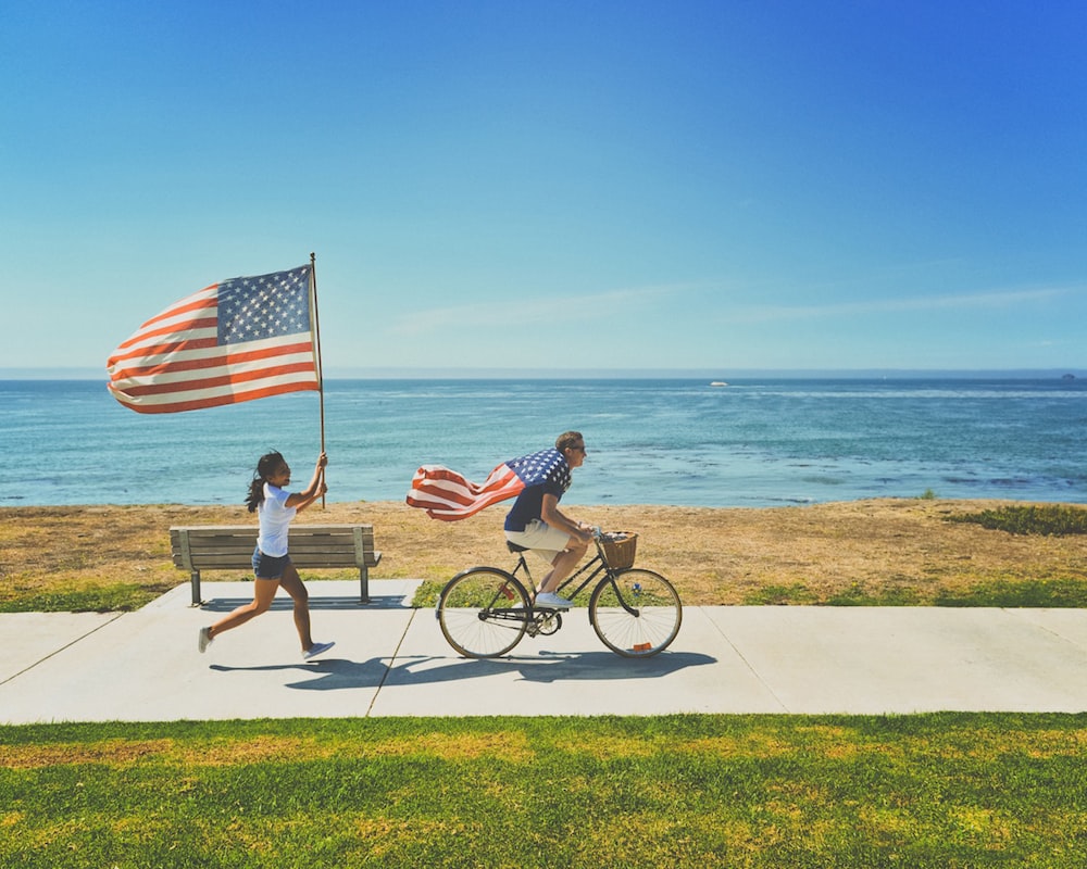 uomo che guida la bici e la donna che corre tenendo la bandiera degli Stati Uniti