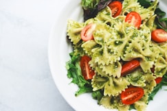 Pesto pasta with sliced tomatoes served on white ceramic plate