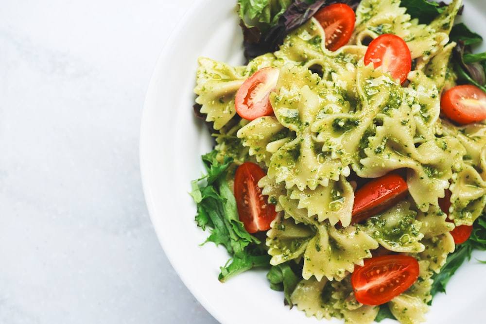 Pesto pasta with sliced tomatoes served on white ceramic plate