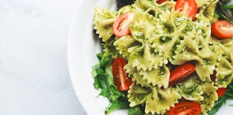 Pesto pasta with sliced tomatoes served on white ceramic plate