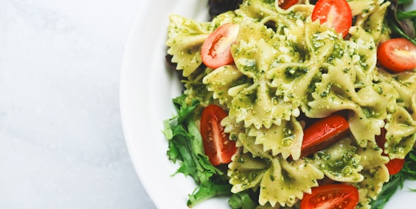 Pesto pasta with sliced tomatoes served on white ceramic plate