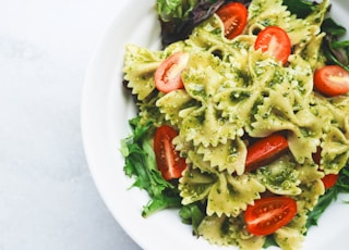 Pesto pasta with sliced tomatoes served on white ceramic plate