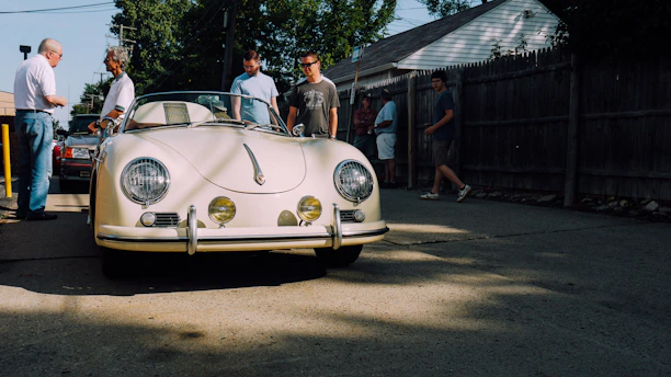 A classic vintage car gathering on a sunny day with smiling owners chatting.