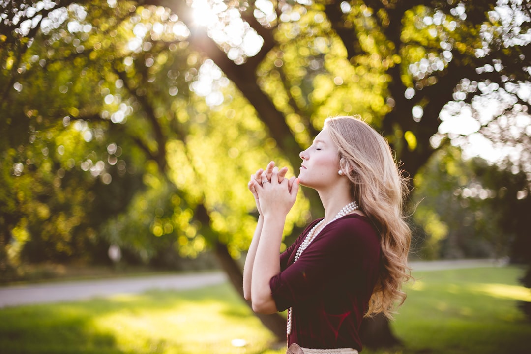 A young blonde woman putting her hands together in a gesture of prayer in a park