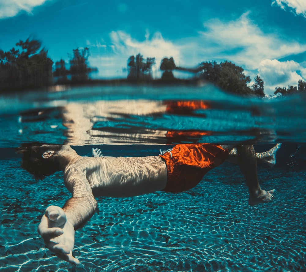 underwater photography of floating man wearing red shorts