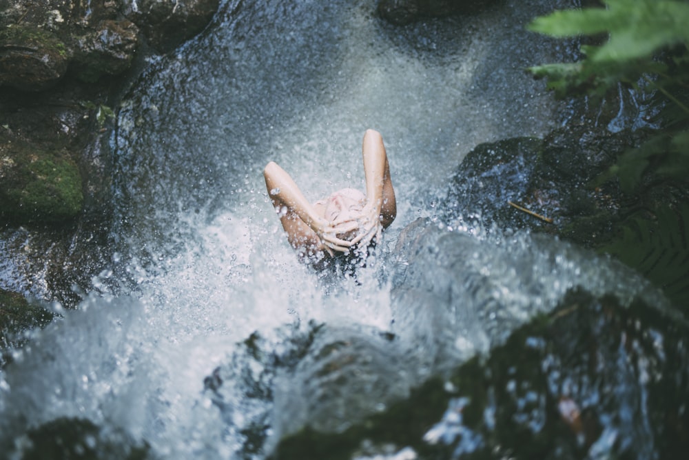 high-angle photography of woman bathing below waterfalls during daytime