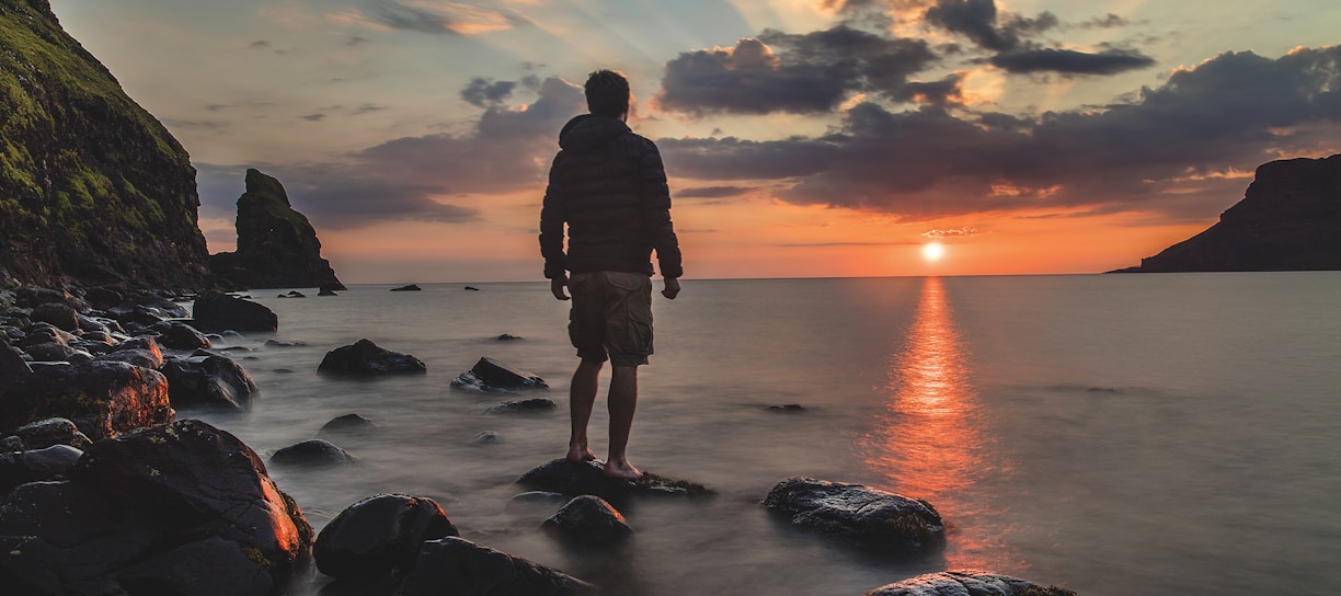 man standing on stone looking at sunset