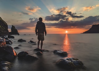 man standing on stone looking at sunset