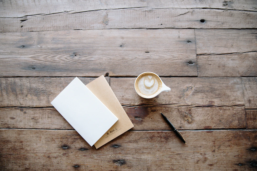 A warm flat-lay of notebooks, a pen and a coffee on a rustic wooden desk