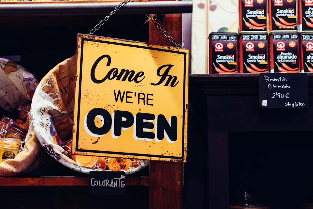 A “Come in, we're open” sign hanging from a railing near the entrance to a store