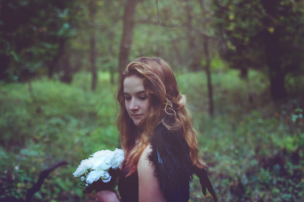 shallow focus photo of woman in black top holding white flowers