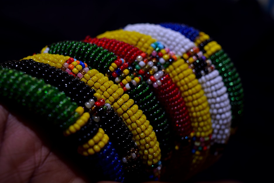 A series of colorful beaded bracelets arranged side by side, showcasing intricate patterns and a variety of vibrant colors including green, red, yellow, white, and blue. The beads are small and densely packed, creating textured and detailed designs.
