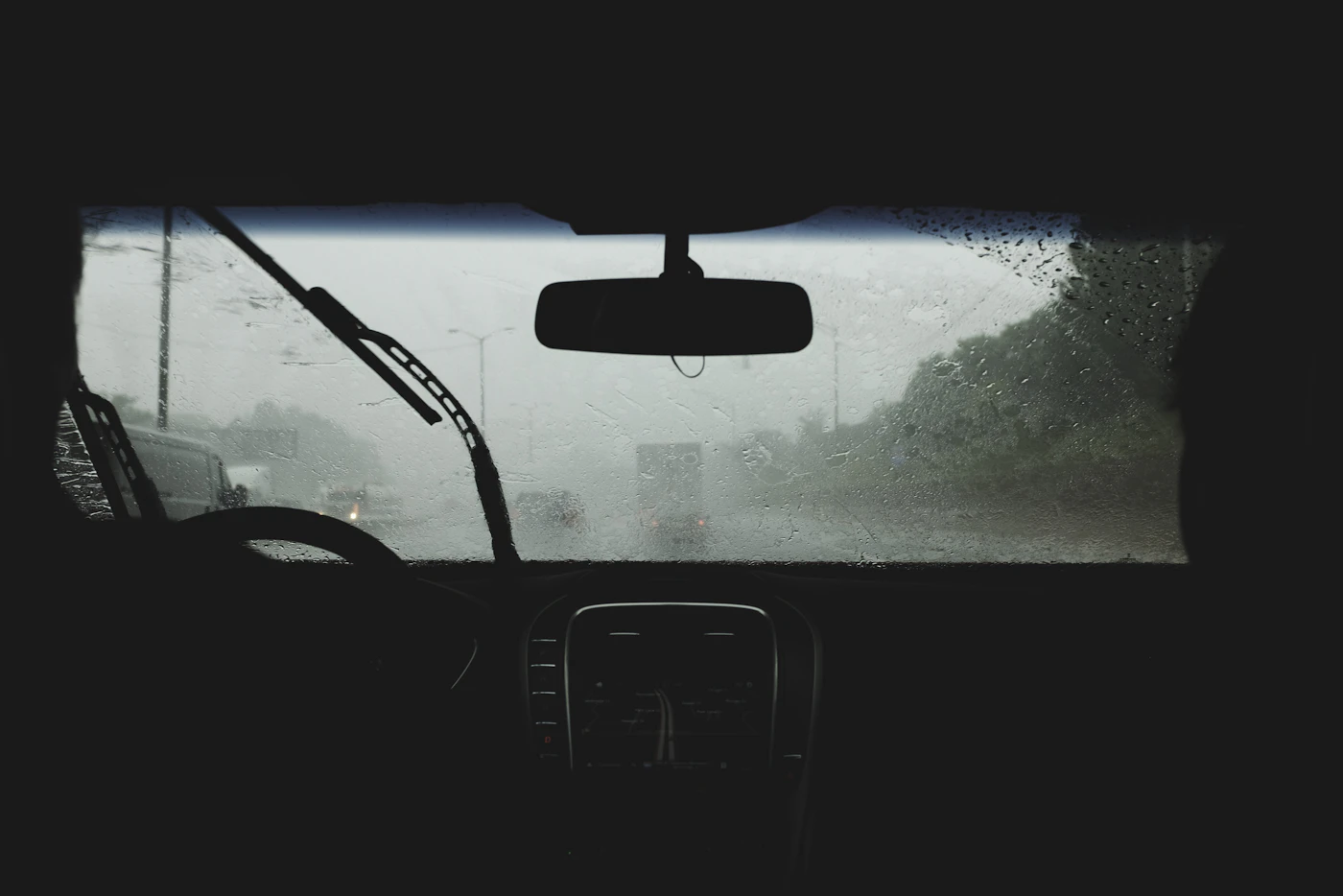 View through a rain-streaked windshield with the wipers running on a wet highway, the kind of drive where New Hampshire driving laws for visitors on headlights and following distance matter