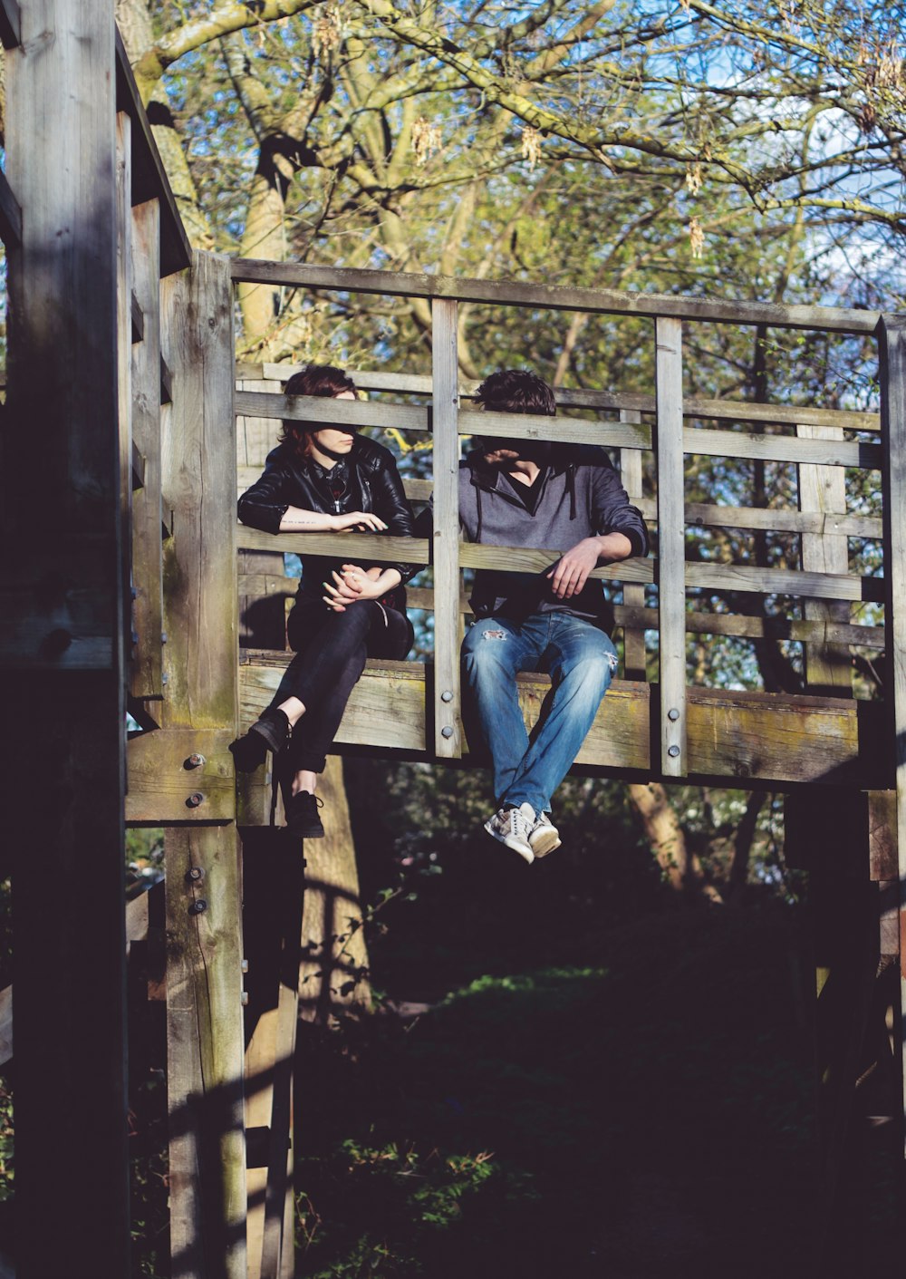 man and woman sitting on side of wooden bridge