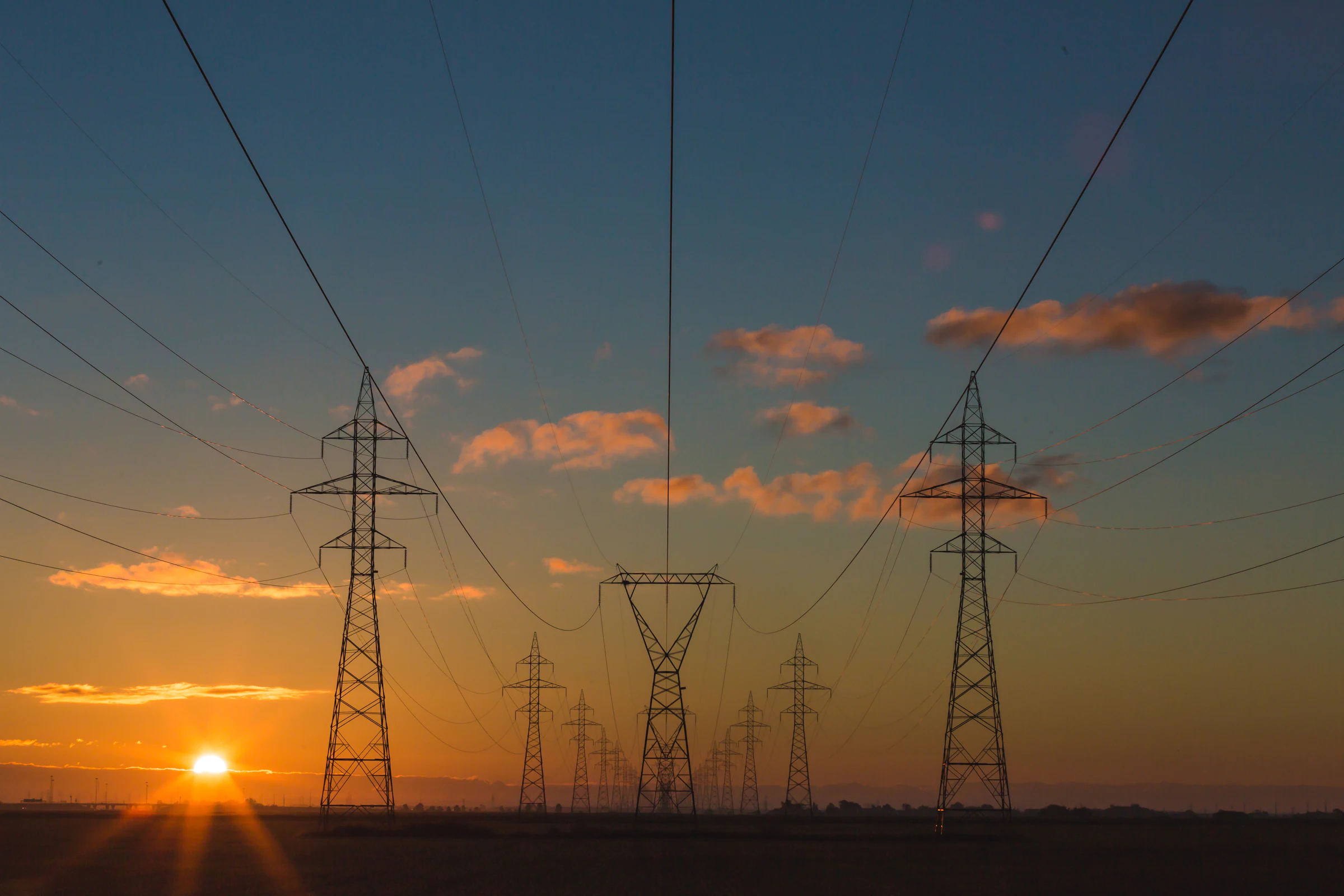 High-voltage transmission towers carrying lines across open country at dusk