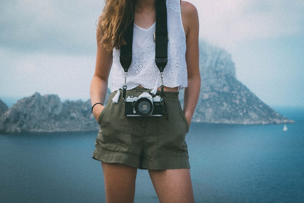 woman wearing green short shorts near body of water with camera at daytime