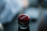 Close-up of a cola bottle cap being popped open with fizz escaping.