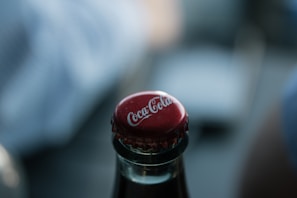 Close-up of a cola bottle cap being popped open with fizz escaping.