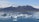 Icebergs float in a serene blue lagoon with a backdrop of snow-capped mountains under a clear sky. A small boat carrying people is navigating through the icy waters.
