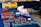 A market stall displays an assortment of fresh berries. Several blue cartons filled with red raspberries are spread out on a dark blue tablecloth. A larger container holds strawberries, and there are white plastic bags containing additional berries. In the background, yellow boxes labeled 'Strawberries' are stacked, adding a bright contrast to the scene.