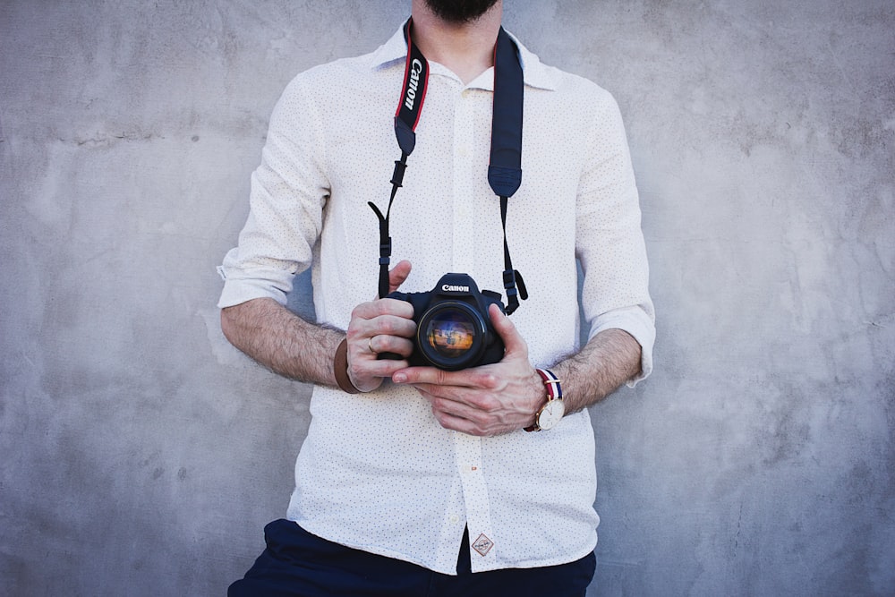 homem na camisa branca do vestido segurando a câmera Canon DSLR