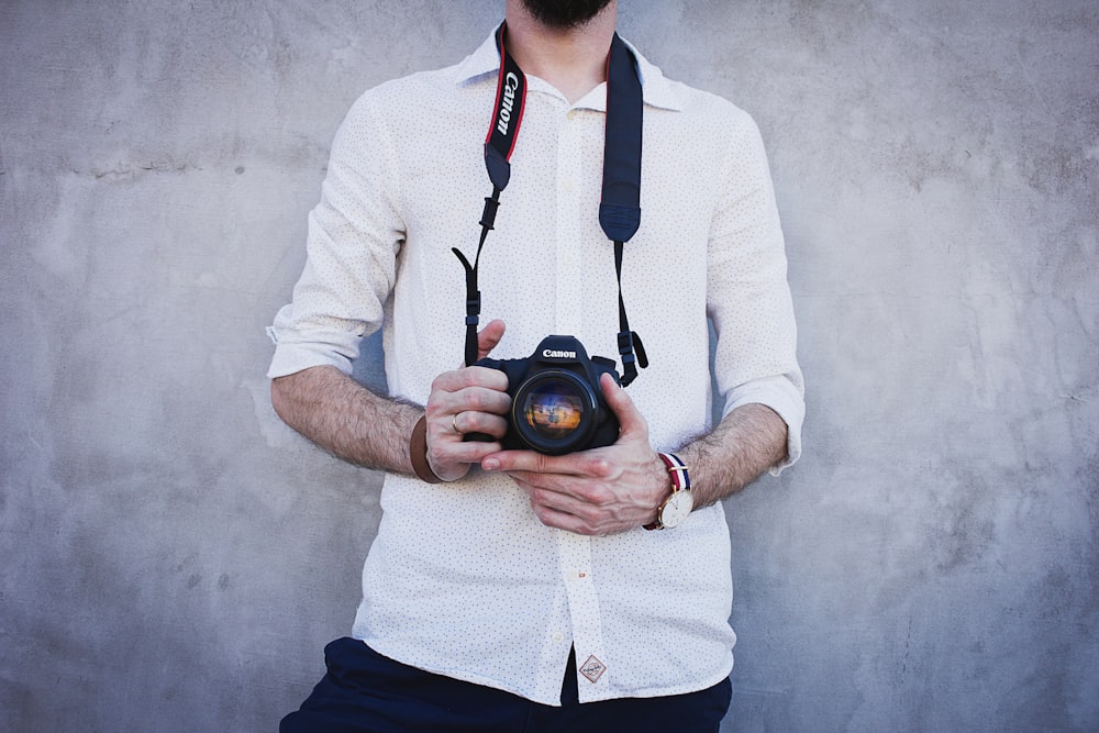 uomo in camicia bianca che tiene la fotocamera reflex digitale Canon