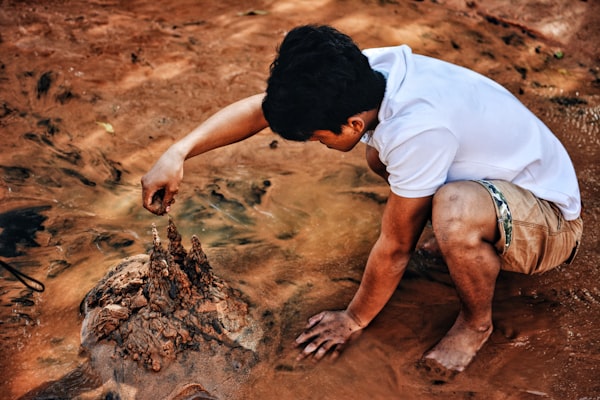 A child crouched in mud, building a small castle.