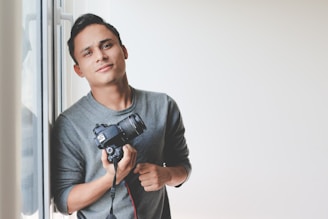 man holding DSLR camera leaning on windowpane