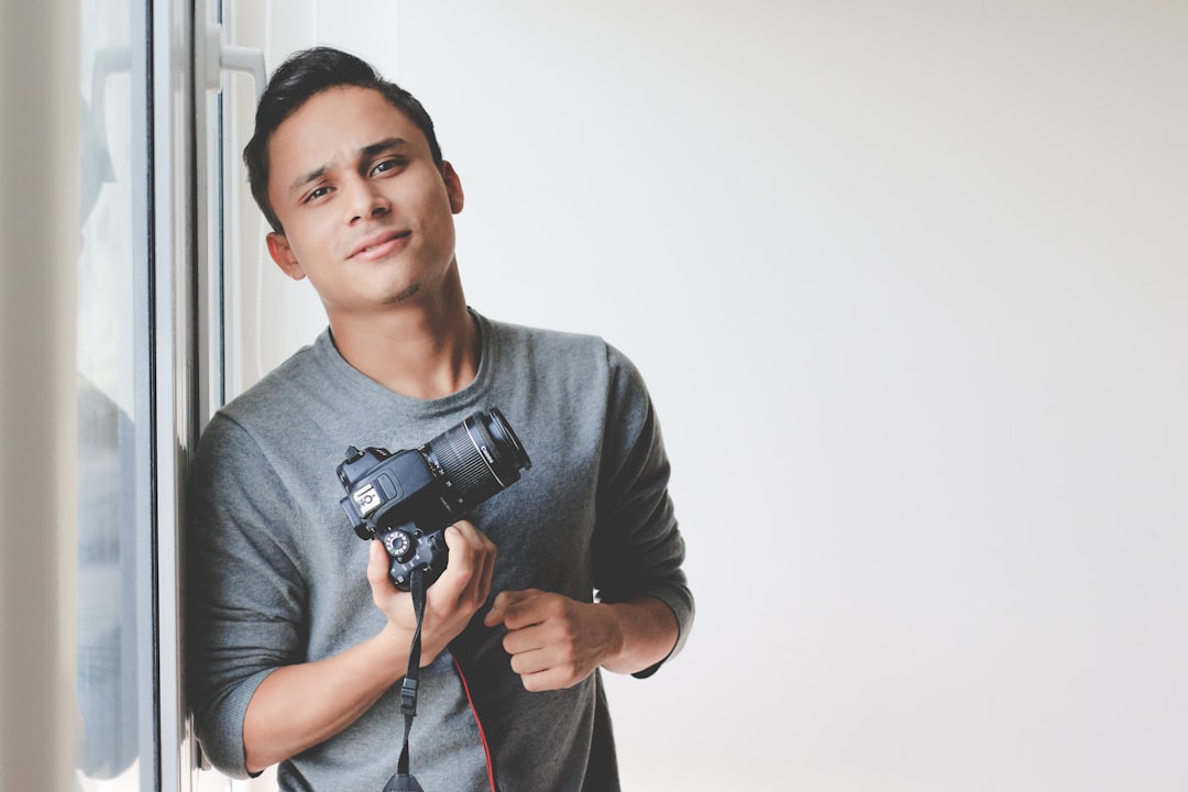 man holding DSLR camera leaning on windowpane