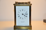 An antique brass carriage clock with a rectangular shape and a white clock face displaying Roman numerals. The casing has a handle on top, and the name 'REED & SON CAMBRIDGE' is visible on the face.