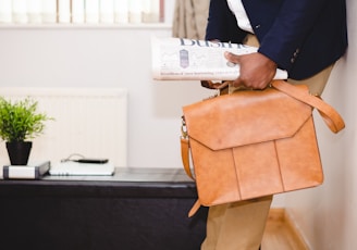 man holding brown leather bag leaning on white wall