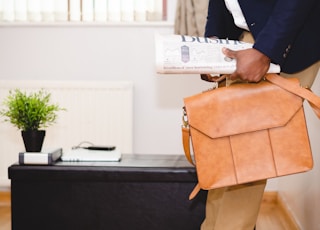 man holding brown leather bag leaning on white wall