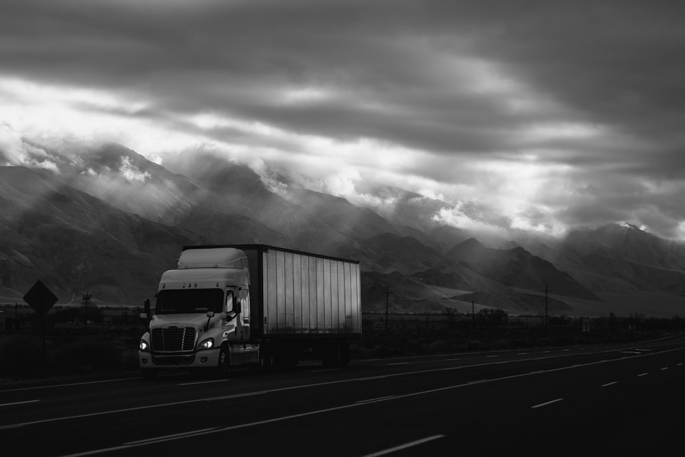 A black-and-white shot of a truck on a road in the mountains