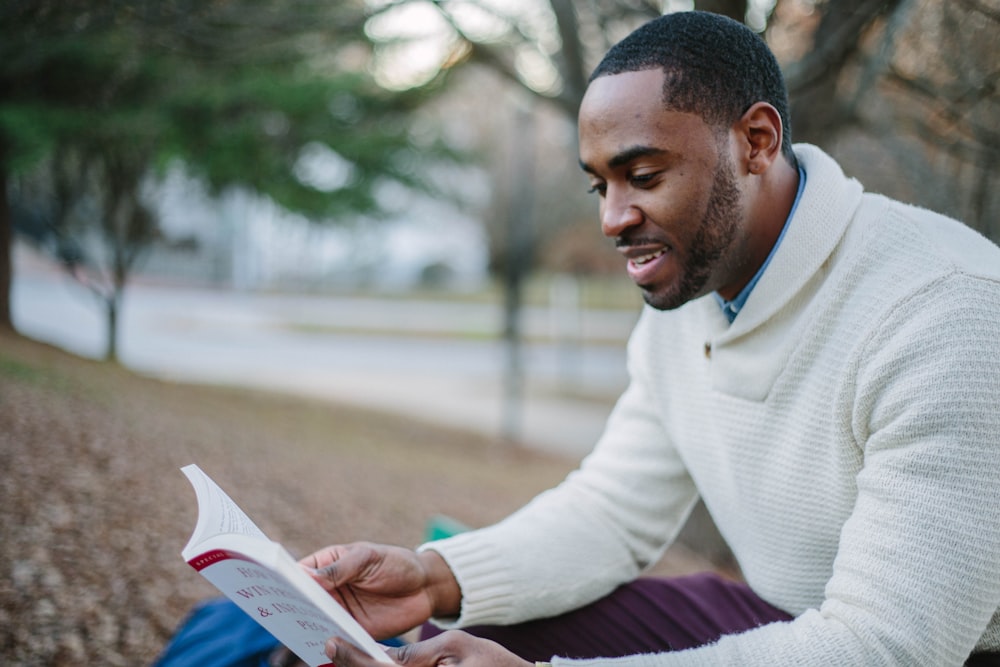 man wearing white sweater while reading book