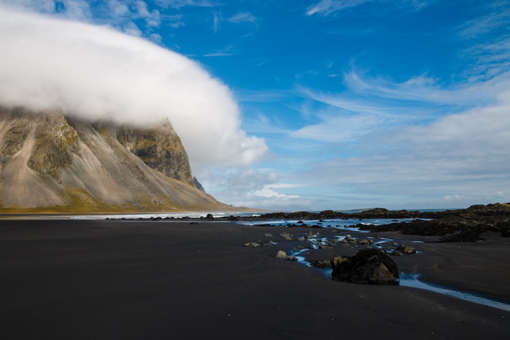 mountain hill covered with clouds near body of water during daytime