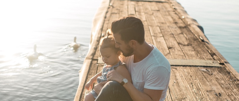 man and girl sitting on brown dock near boat and two white ducks during daytime