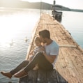 man and girl sitting on brown dock near boat and two white ducks during daytime